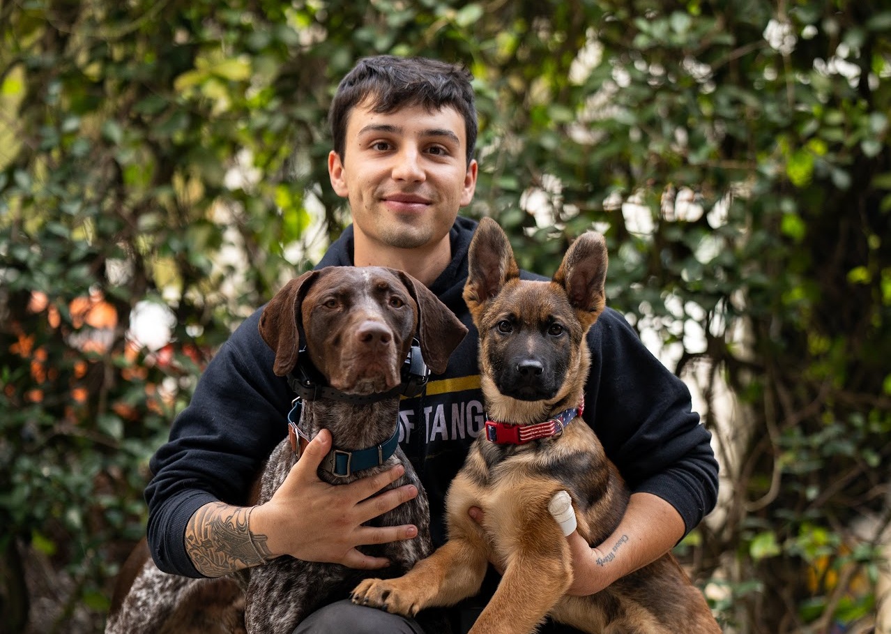 Woof Tang K9 dog trainer posing with a German Shorthaired Pointer and German Shepherd puppy.